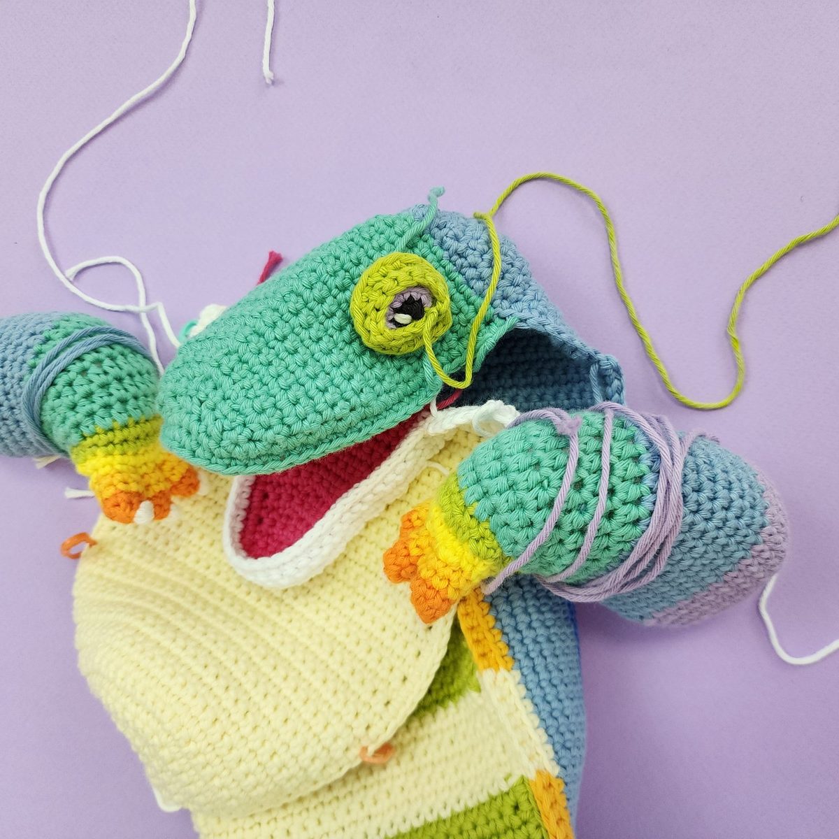 A crochet frog puppet in progress with yarn tails still attached
