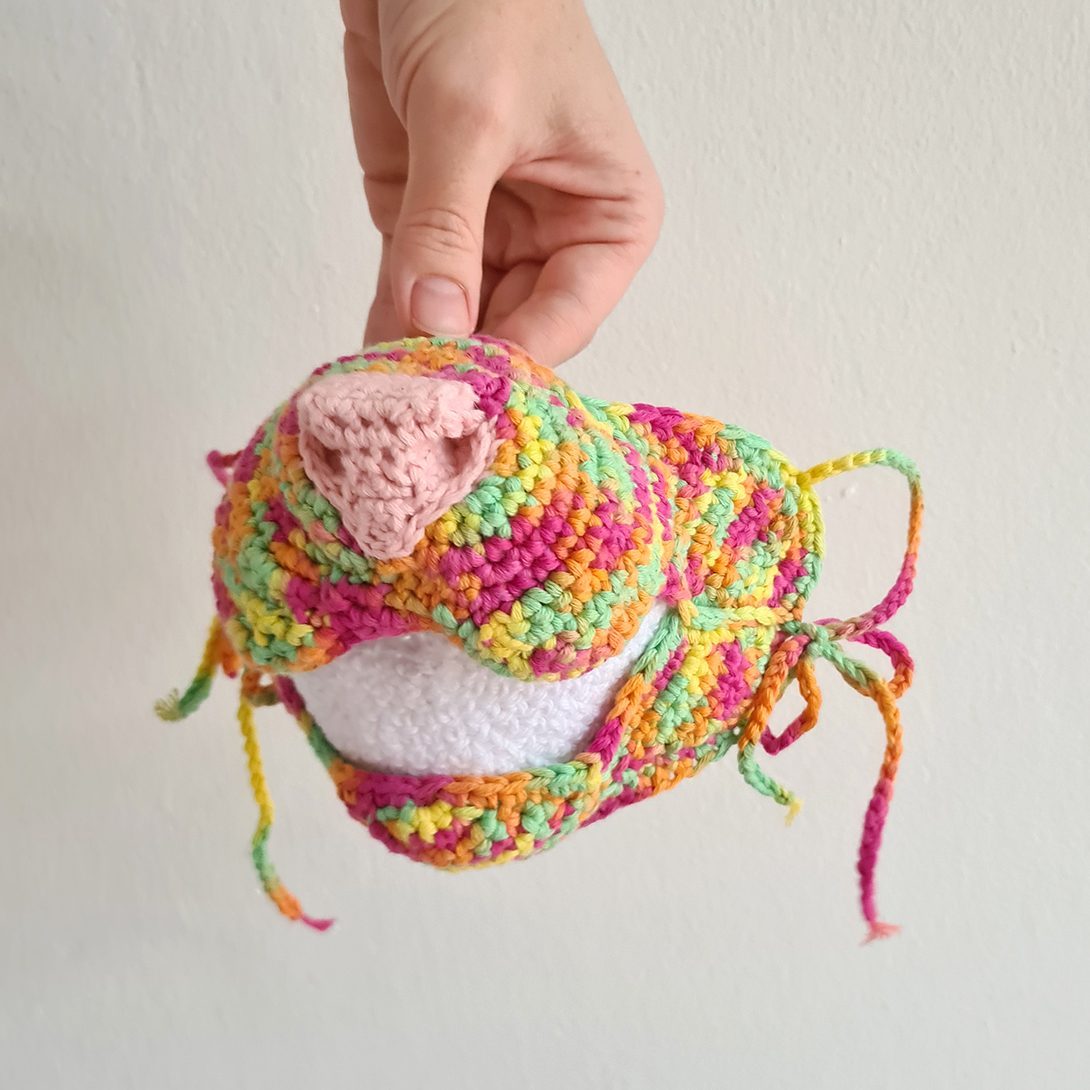 A crochet pig head in progress, held in Jessie's hand with loose yarn ends