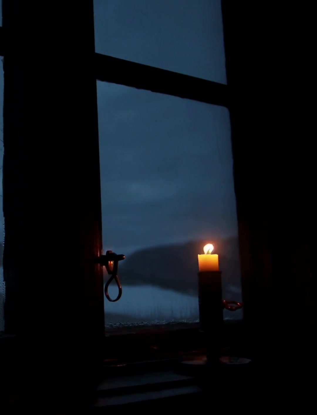 A candle burning in a window at dusk in winter