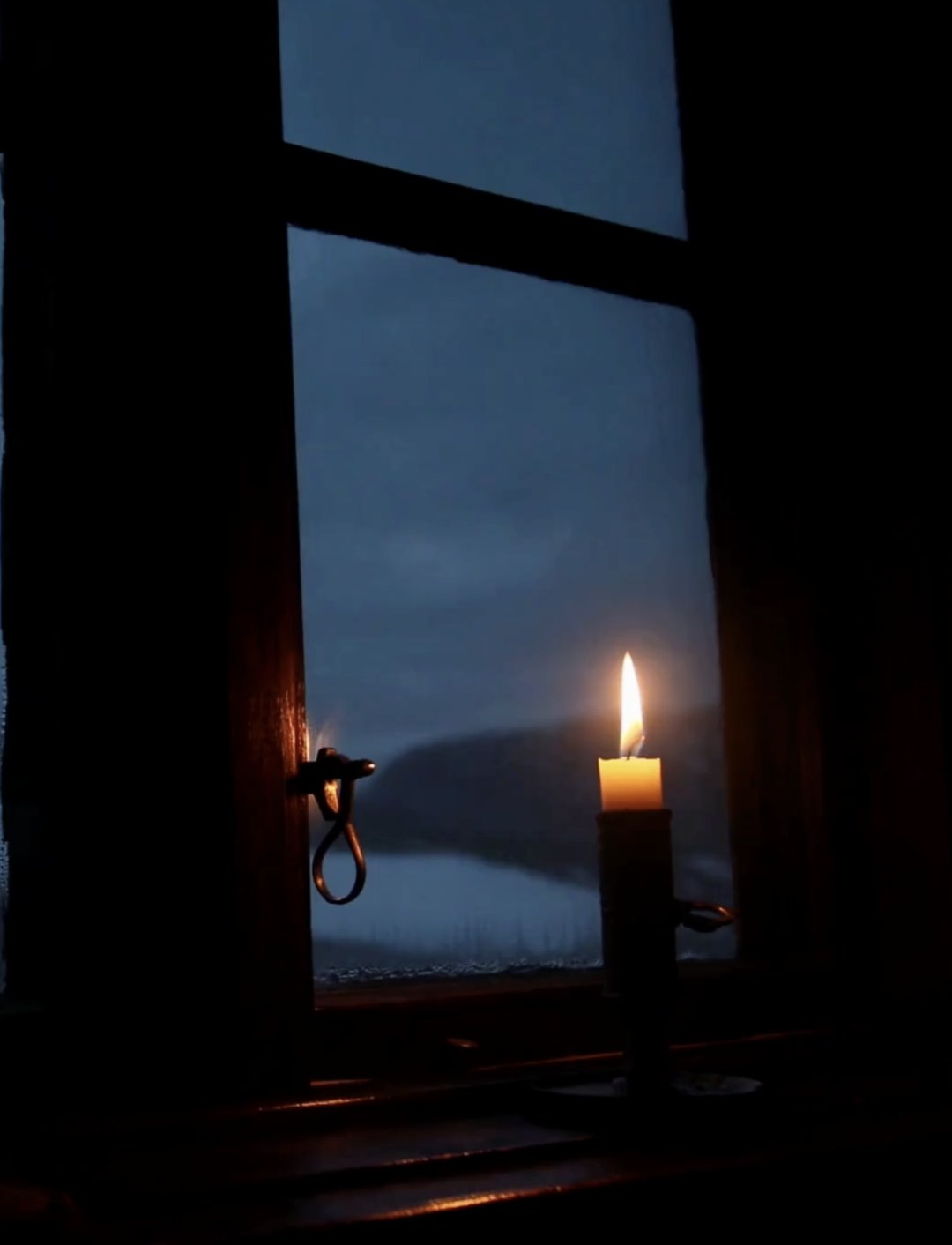 A candle burning in a window at dusk in winter