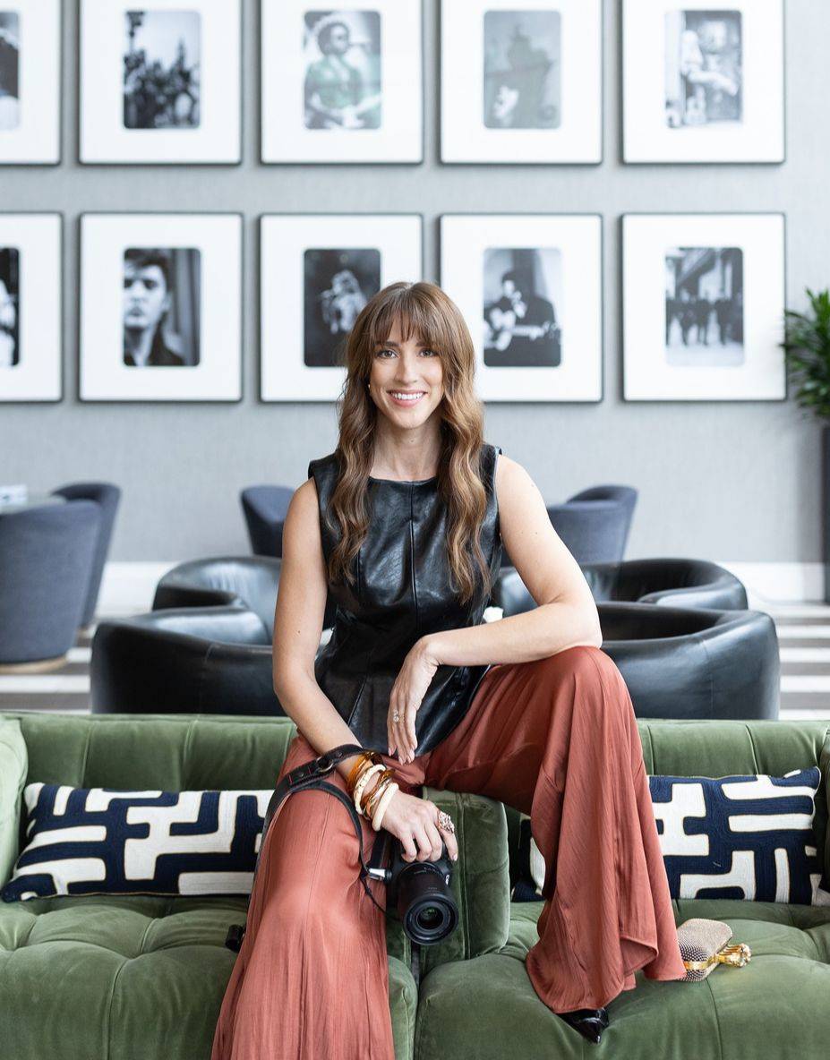 Vanessa Joy sitting with her camera in a lounge with a black-and-white photo gallery wall