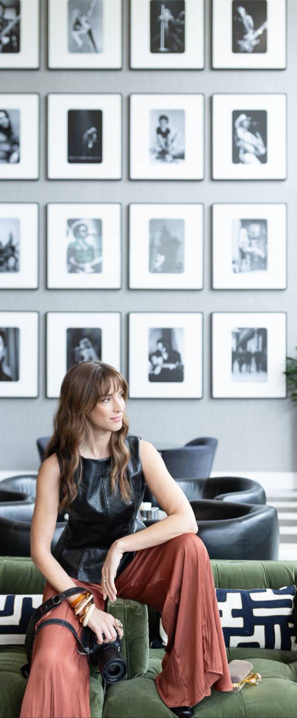 Vanessa Joy sitting with her camera in a lounge with a black-and-white photo gallery wall