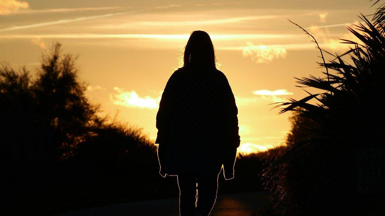Silhouette of a person walking alone on a path at sunset