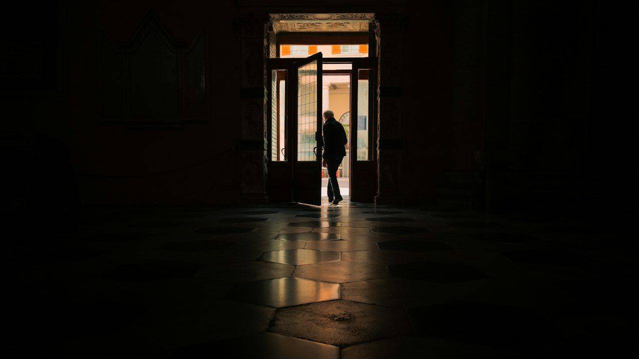 Silhouette of a person standing in a bright doorway at dusk