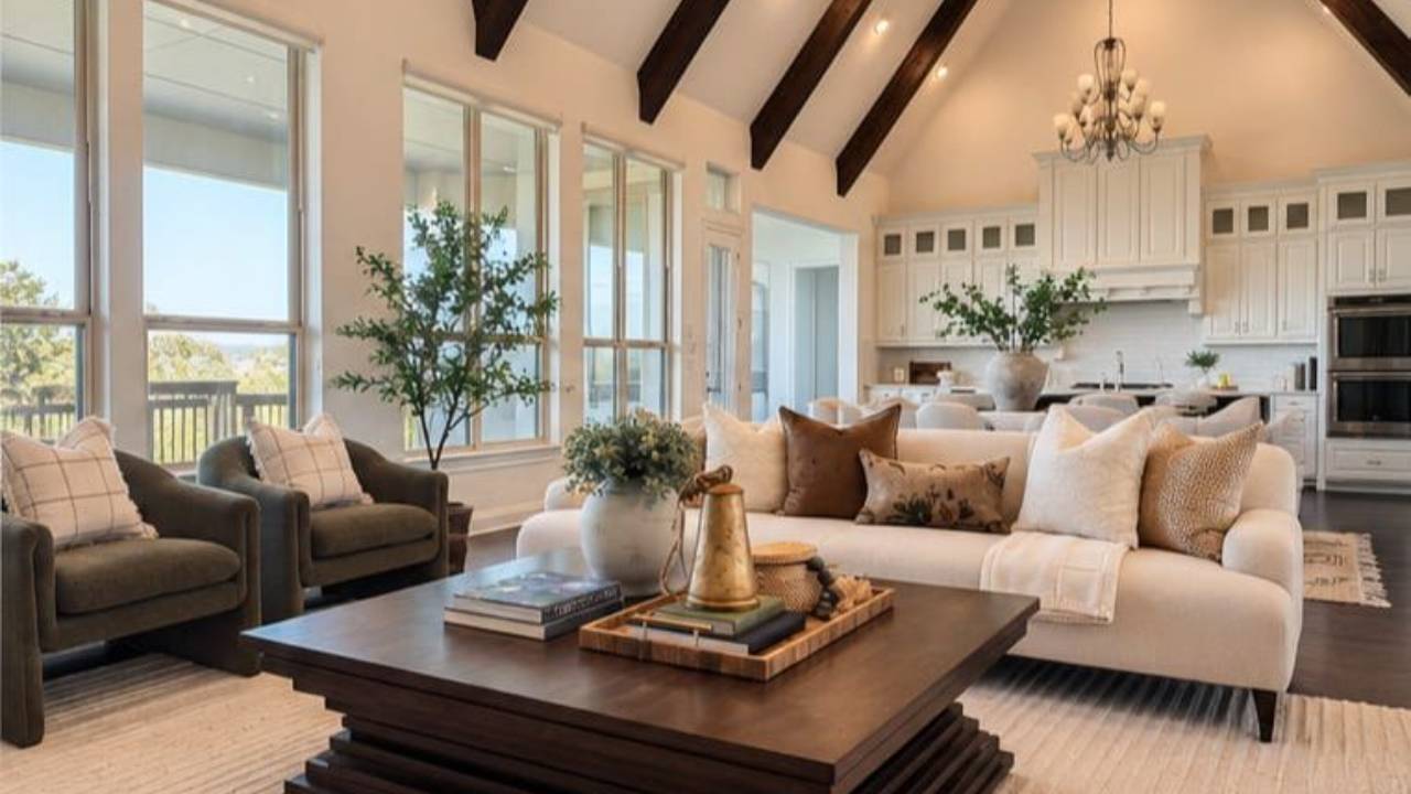 Bright living room with a cream sectional, dark wood coffee table, and open kitchen beneath vaulted ceilings.