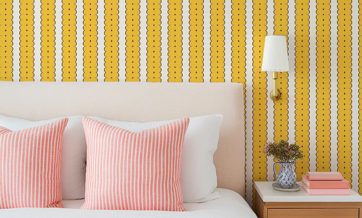 Modern bedroom featuring bold yellow wallpaper, striped pillows, and a bedside table with lamp and decor