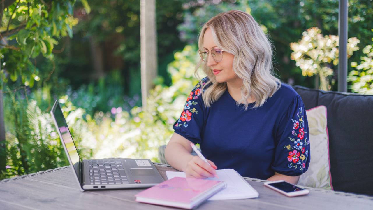 Cathy working on her laptop and taking notes outdoors for her ecommerce business.