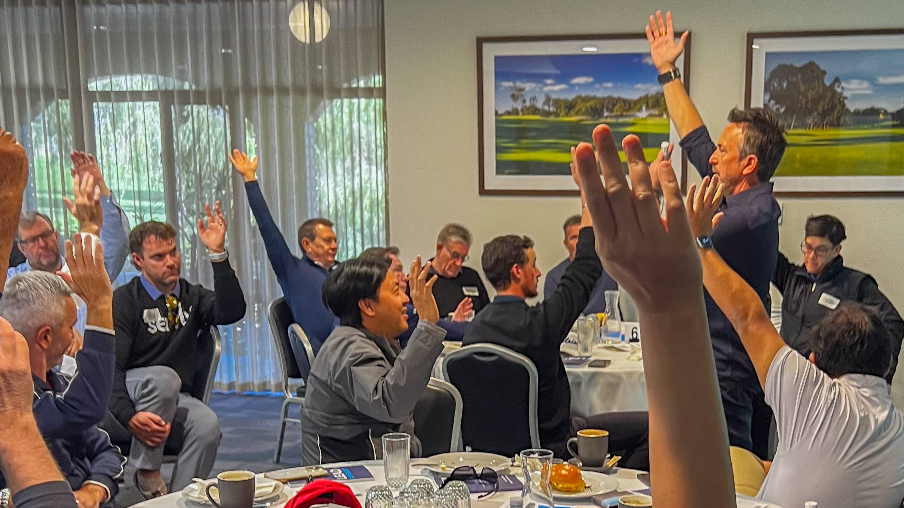 Dave Clare and workshop participants raise their hands during an interactive session.