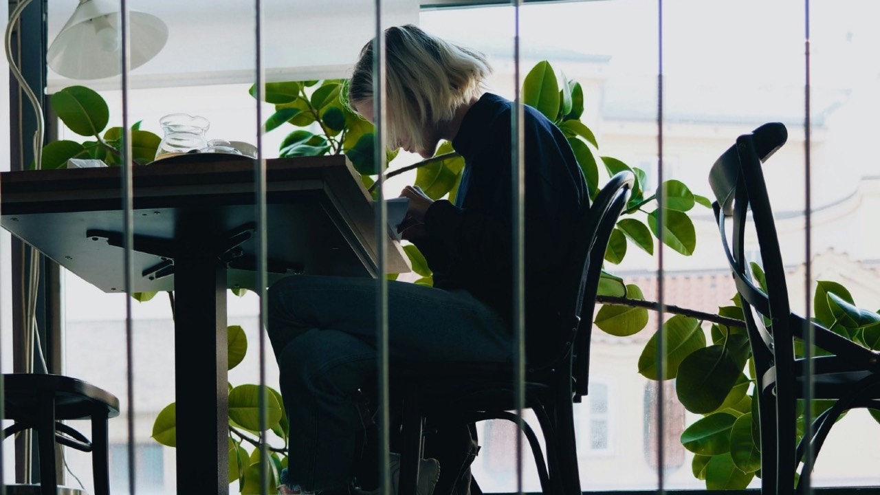 Woman sitting alone at a café table by the window, feeling alone even in a room made for company