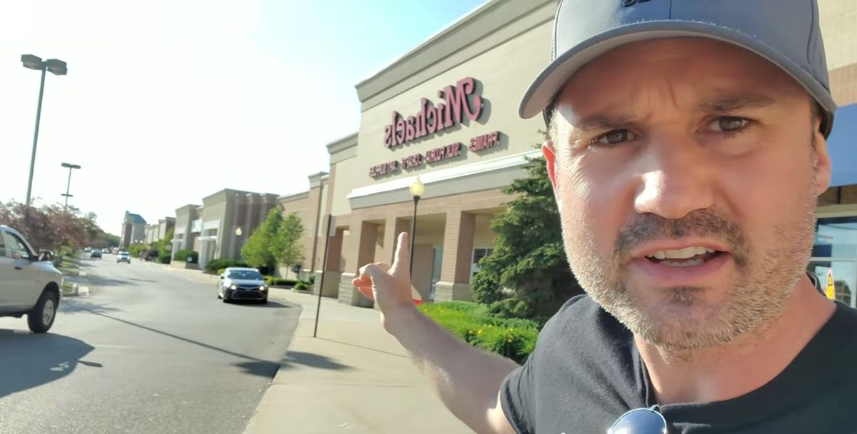 Keith Kalfas on a sidewalk outside a strip mall, pointing down the row of storefronts.