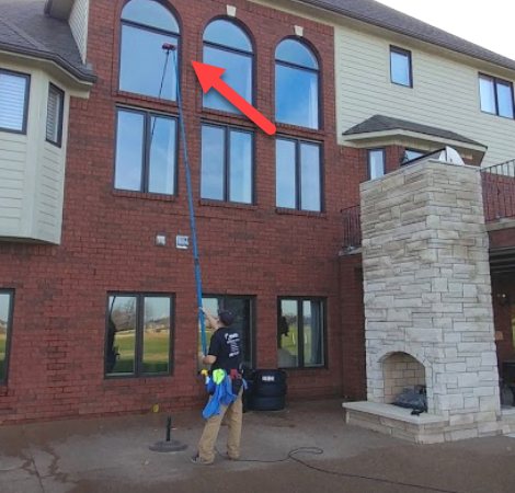 Keith cleaning second-storey windows from the ground with a water-fed pole at a large brick house.