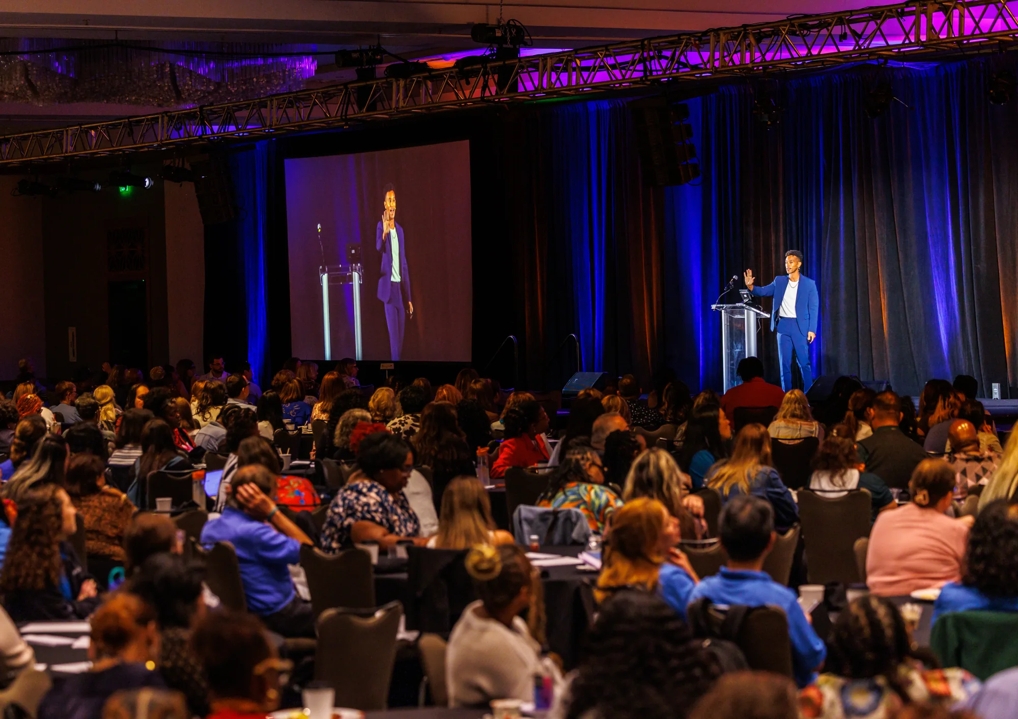 Justin Michael Williams speaking from the stage to a large audience