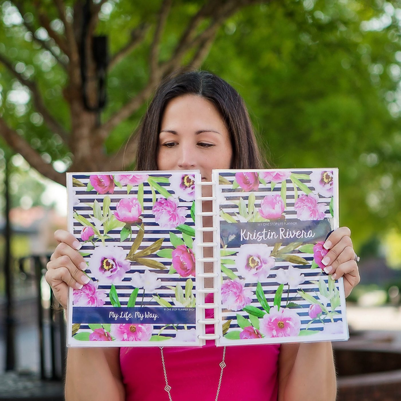 Kristin peeking over the top of her open One Stop Life Planner with a pink and navy floral cover