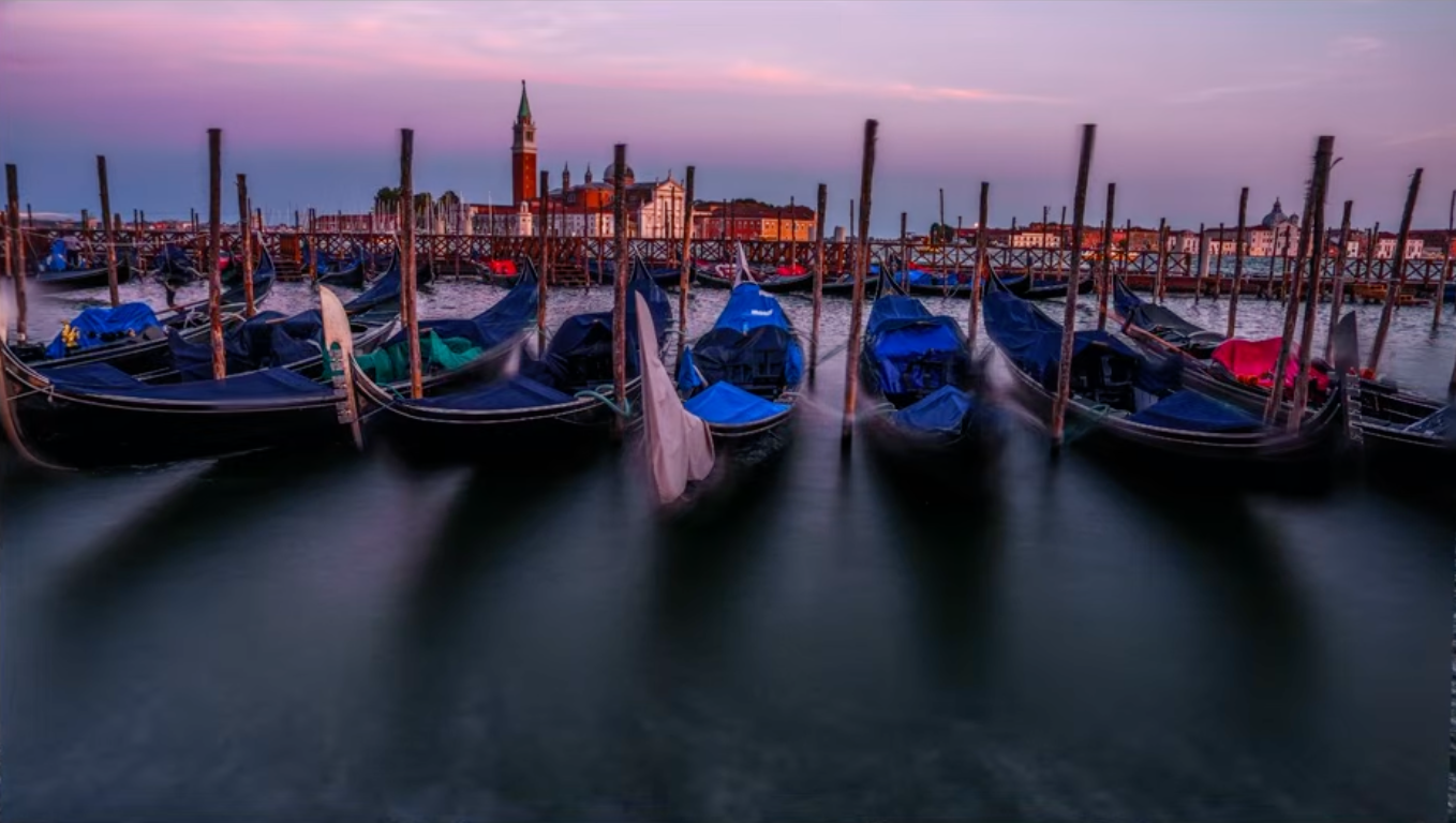 Gondolas moored in Venice at dusk with a pink sky