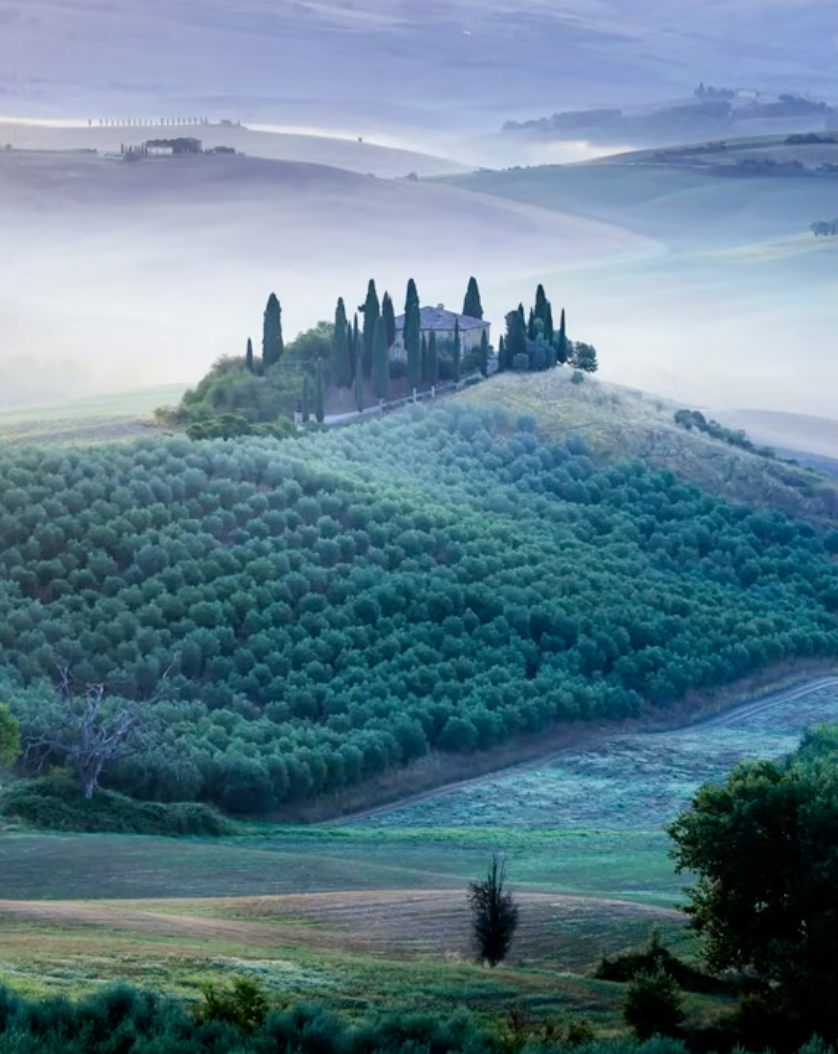 A Val d'Orcia farmhouse on a hilltop surrounded by morning mist in Tuscany