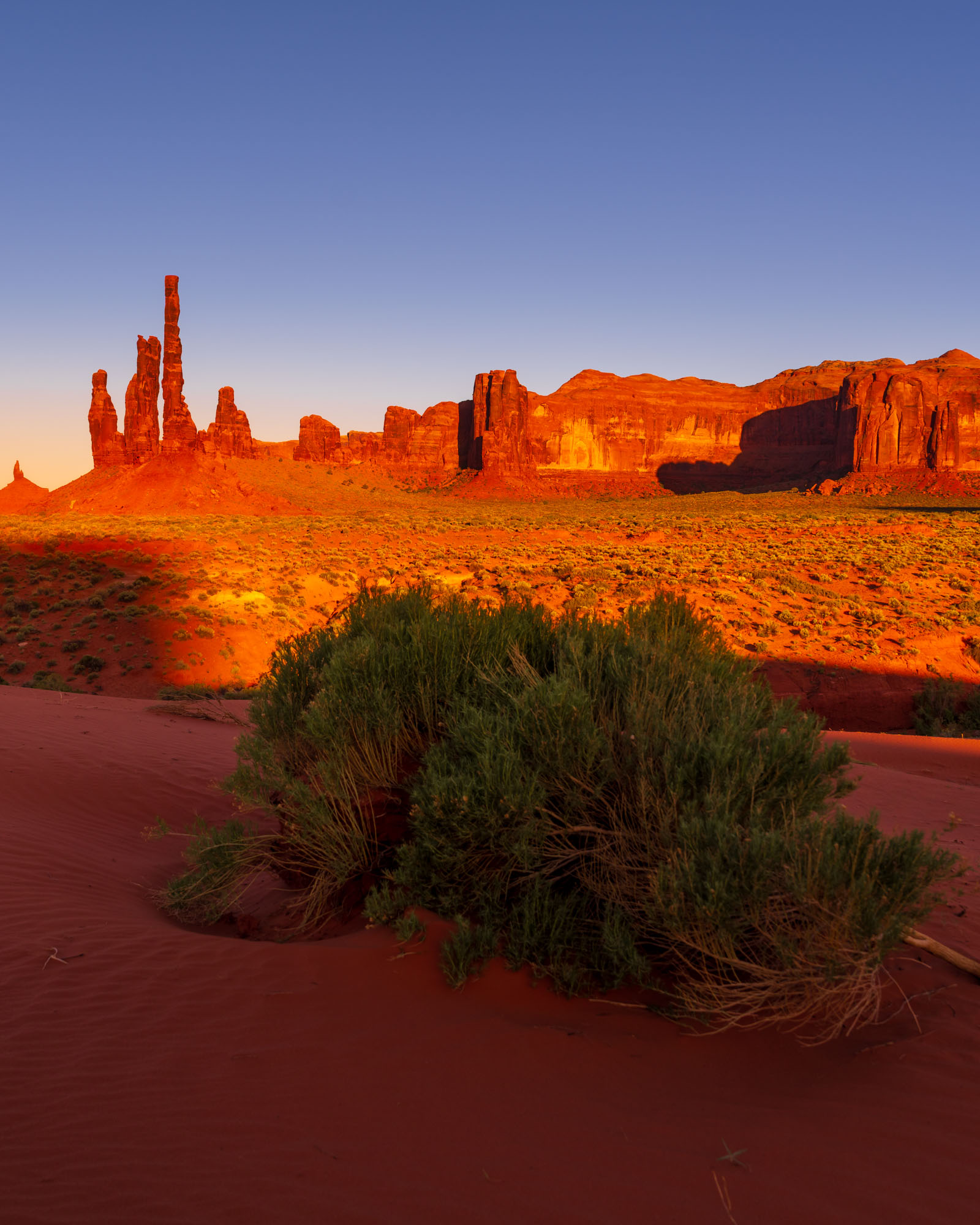 The Totem Pole rock spire at golden hour in Monument Valley with red sand dunes