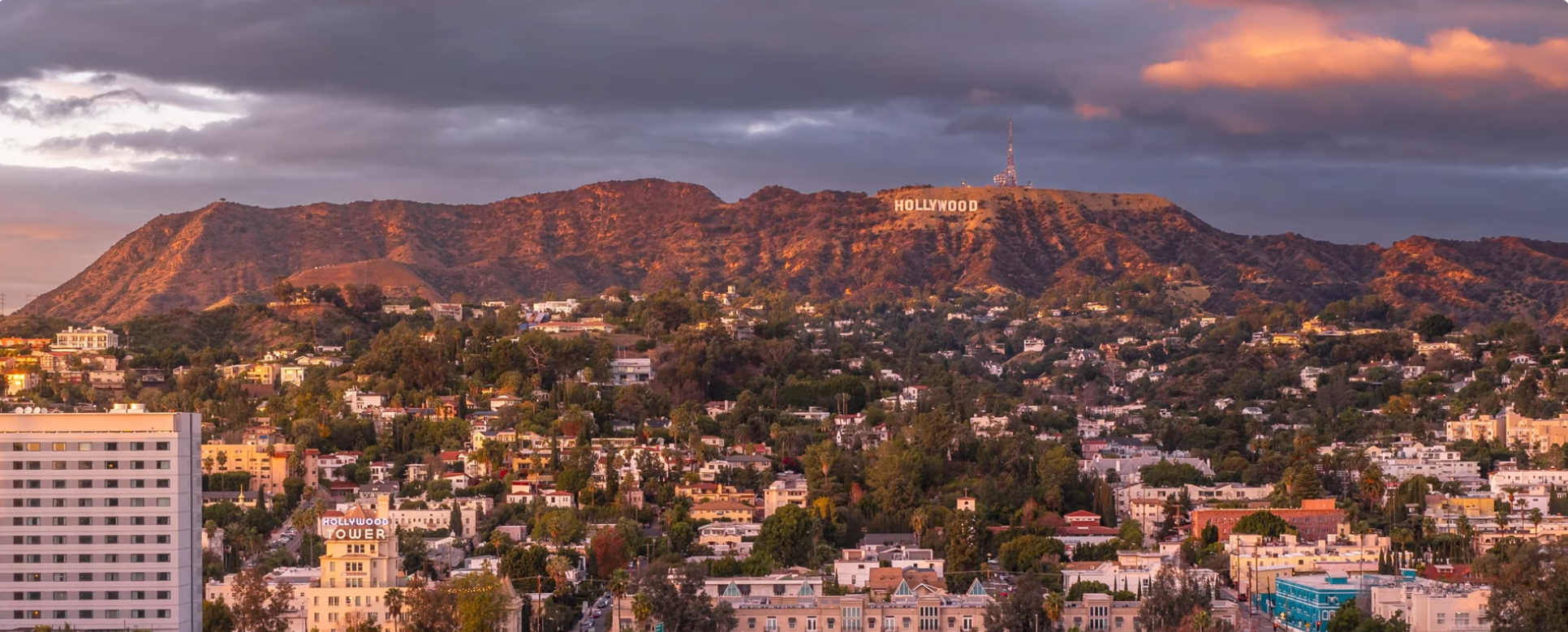 The Hollywood Sign small on the hillside at sunset, seen from a distance with the city below, Los Angeles