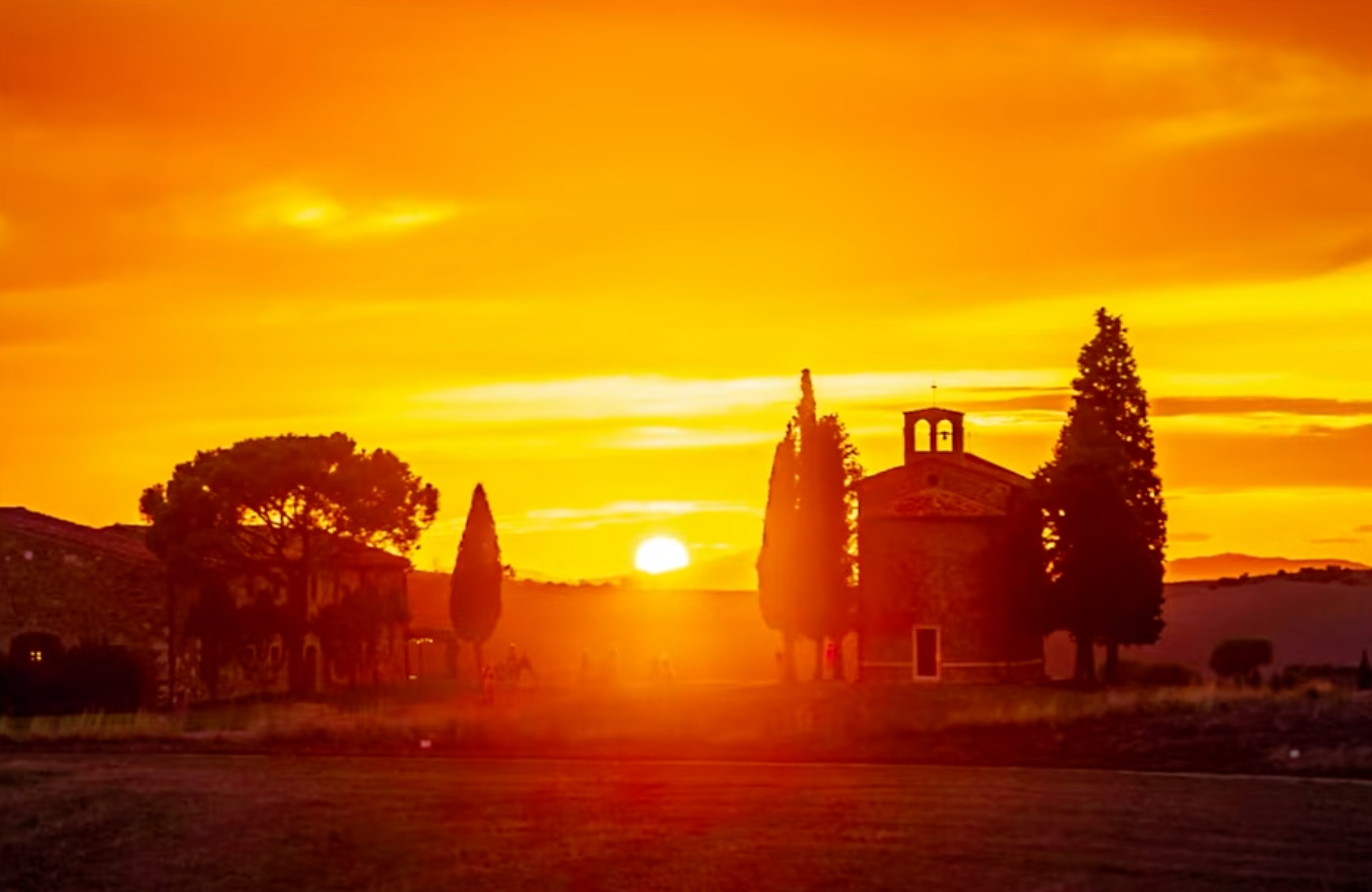 Tuscany at sunset, a church and cypress trees silhouetted against a golden sky