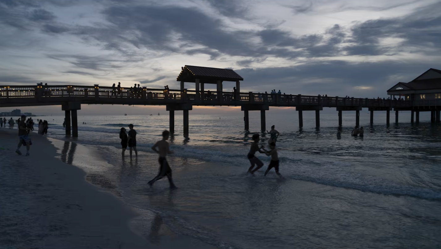 A crowded pier at sunset with people running through the water before the long exposure