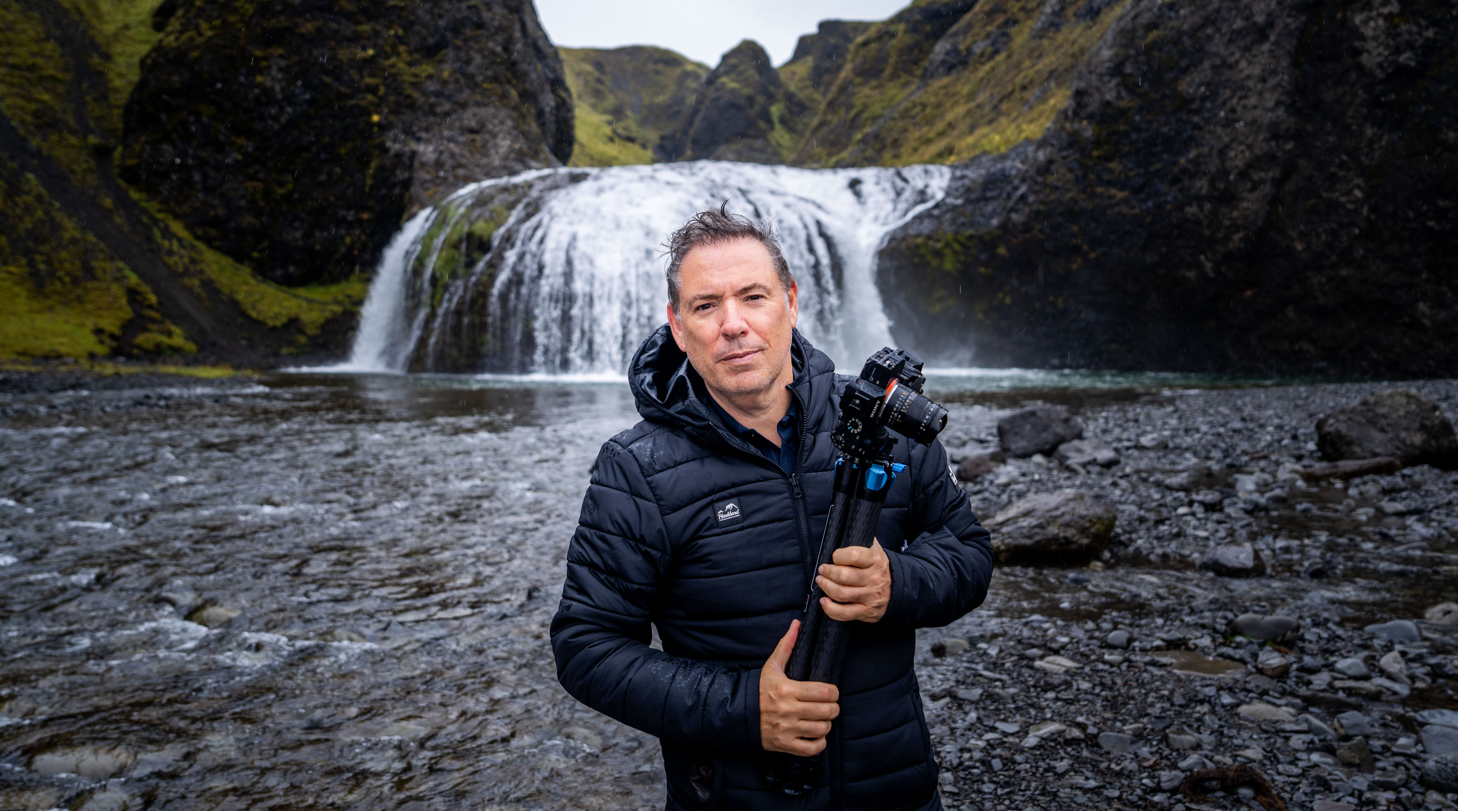 Serge Ramelli standing in front of an Iceland waterfall holding his camera