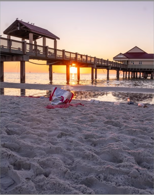 A pier at sunset ruined by a piece of trash in the sandy foreground
