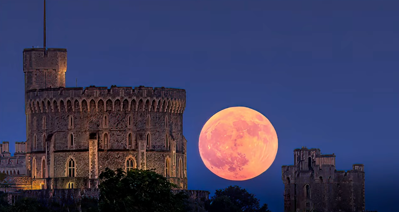 A large orange supermoon rising beside the round tower of Windsor Castle at dusk