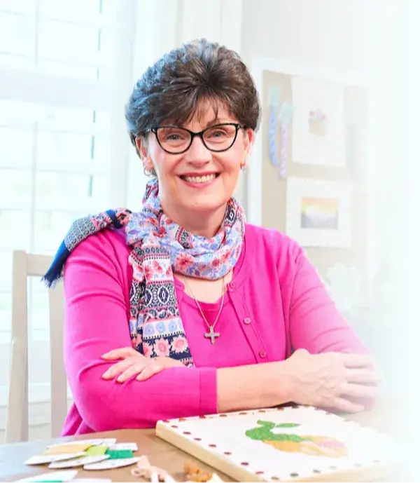 Ellen Johnson, needlepoint expert, smiling at her stitching table
