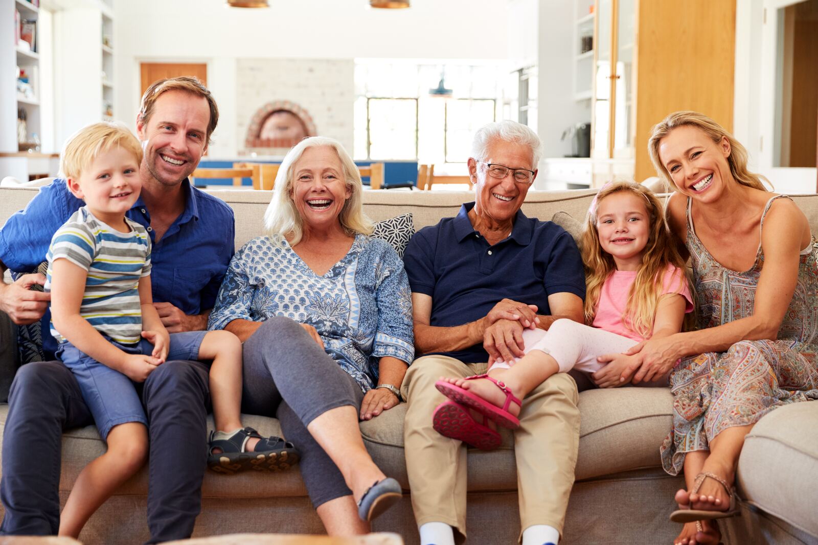 Three generations of a family smiling together on a sofa at home, representing Canadian immigration for families