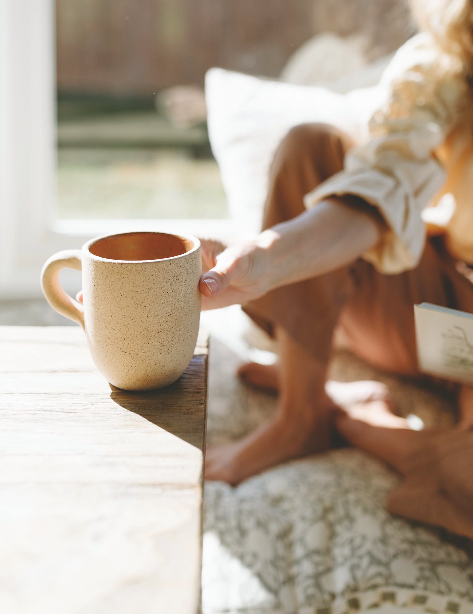 A ceramic mug of coffee held in the morning light, a cozy afternoon of reading ahead