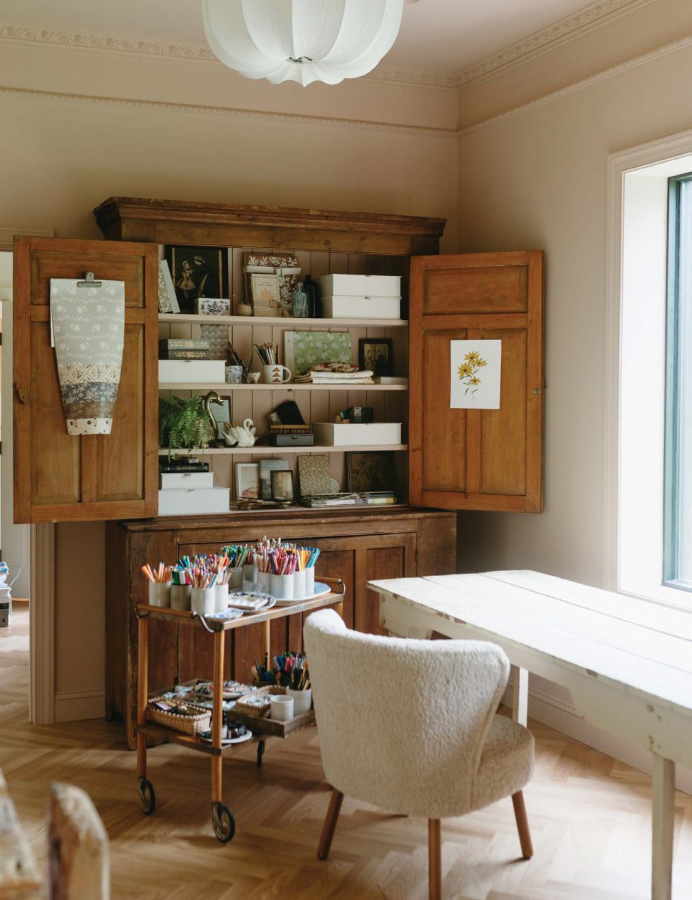 The analog studio: an antique wooden cabinet of supplies, a white desk by the window, and a bar cart of paints