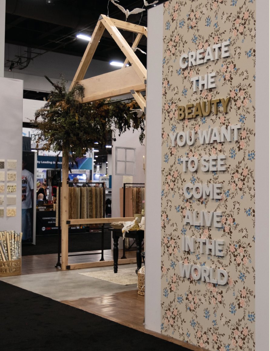 Plaster birds flying above the booth entrance beside a patterned wall that reads Create the beauty you want to see come alive in the world