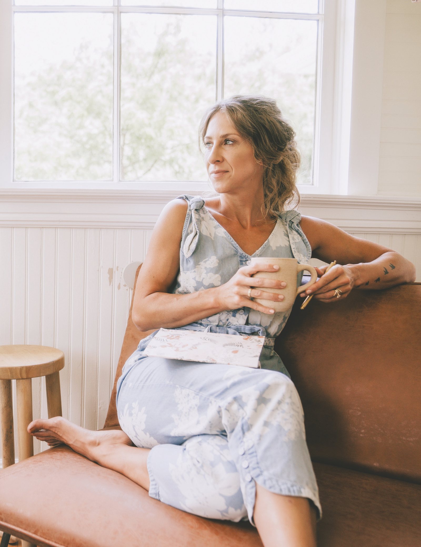 Bonnie Christine curled up in an armchair with a book and a mug, sunlight through the window