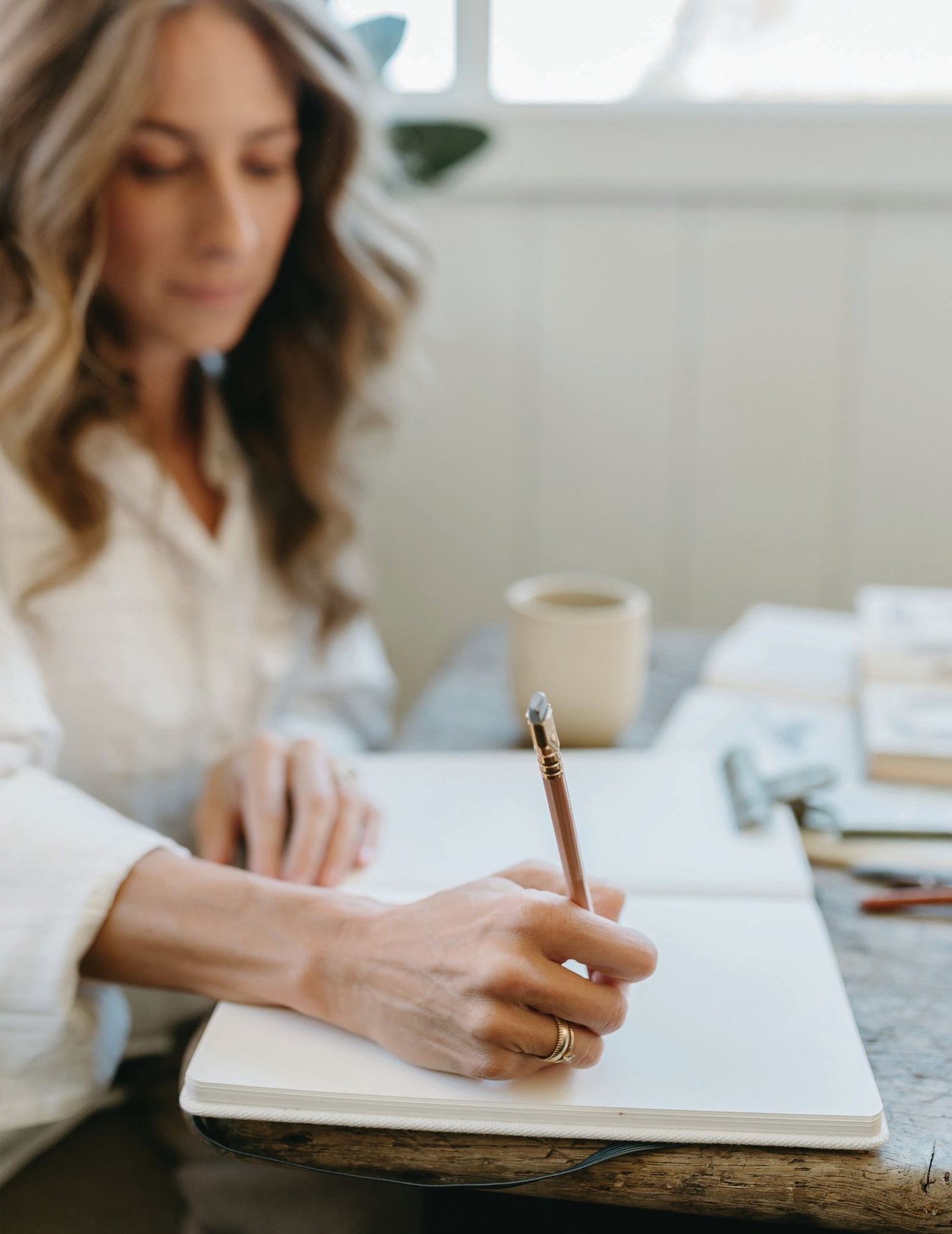 Bonnie Christine writing in a notebook at a wooden desk by a window