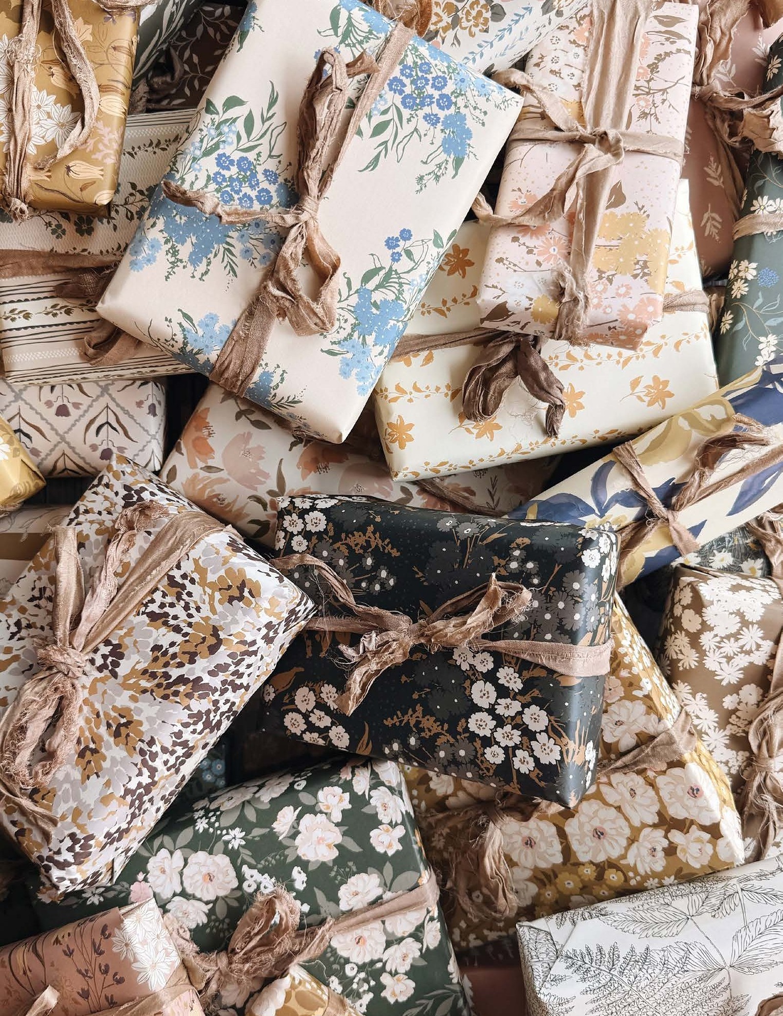 A pile of presents wrapped in Bonnie Christine's patterned gift wrap and tied with ribbon