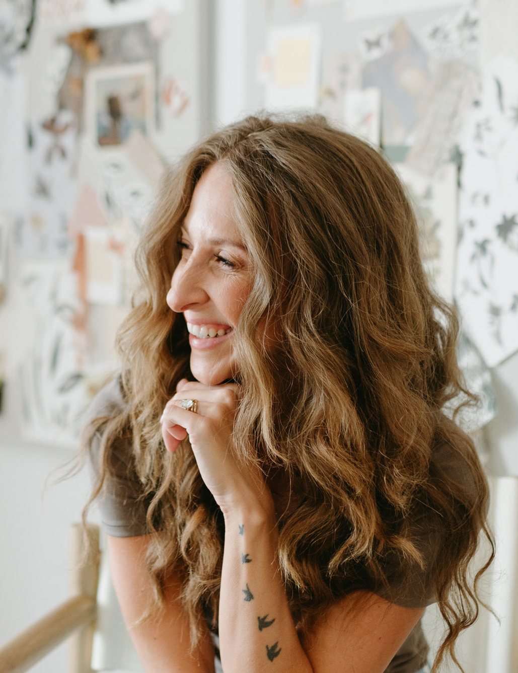Bonnie Christine laughing at her desk, a wall of pinned inspiration behind her