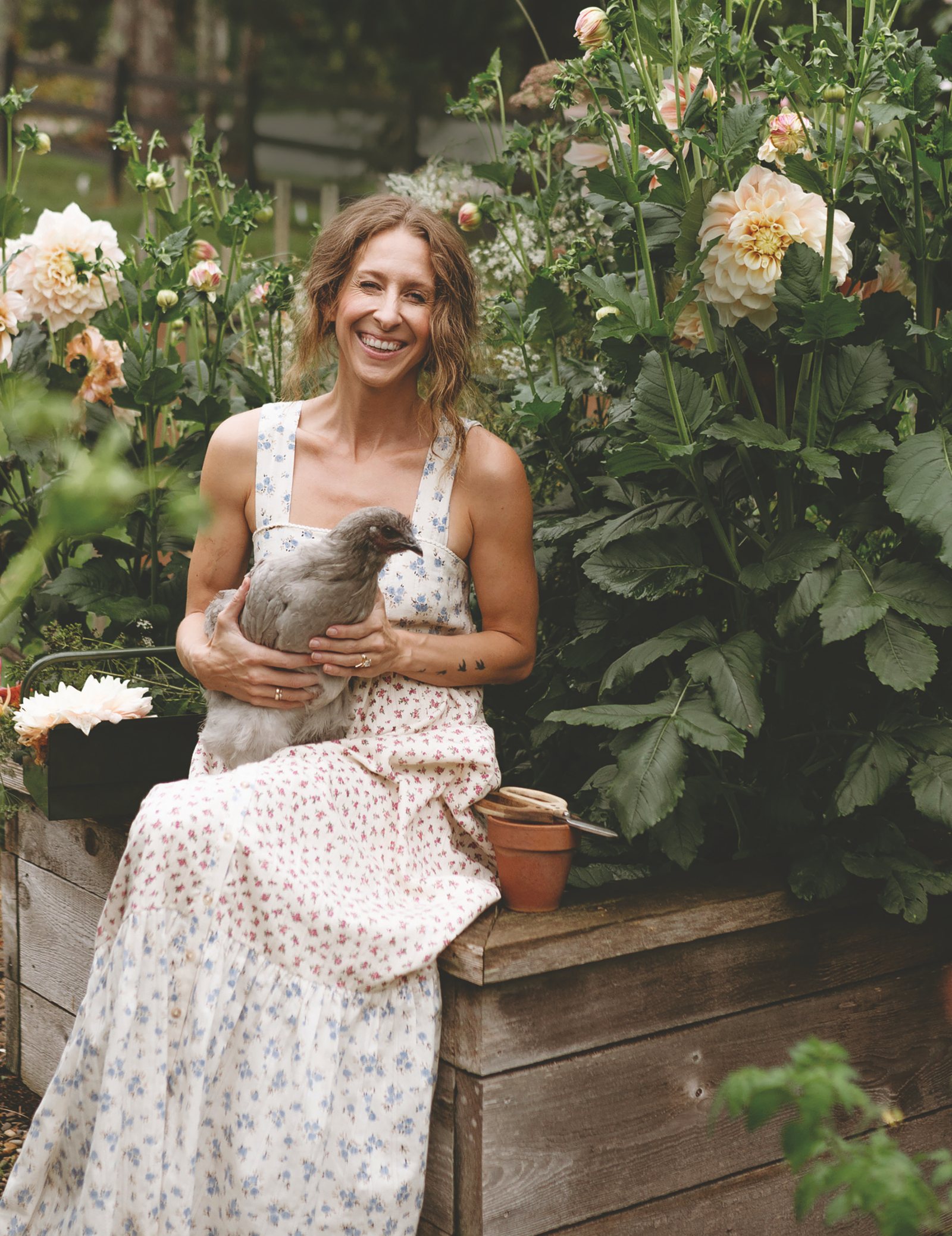 Bonnie Christine in a floral dress holding a hen in her garden
