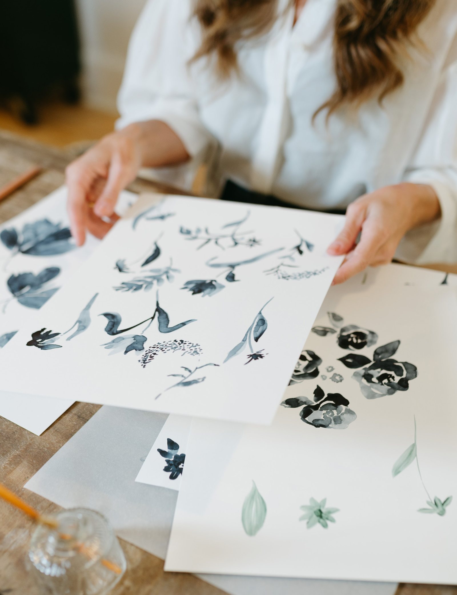 Bonnie Christine laying out hand-painted indigo botanical motifs on a wooden table