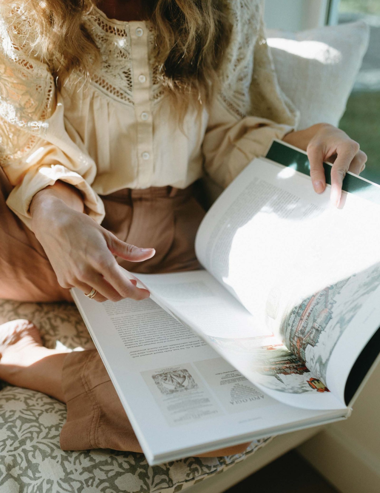 Bonnie Christine in a cream sweater turning the pages of a book in her lap