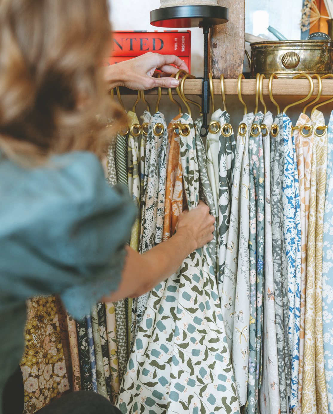 Bonnie Christine flipping through fabric swatches of the finished collection on brass hangers