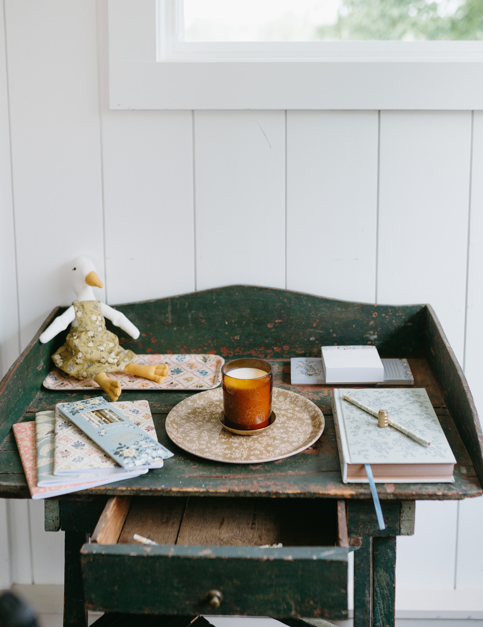 A vintage green desk styled with Flowerie products: a Birdie duck doll, an amber candle, floral notebooks, and a patterned tray