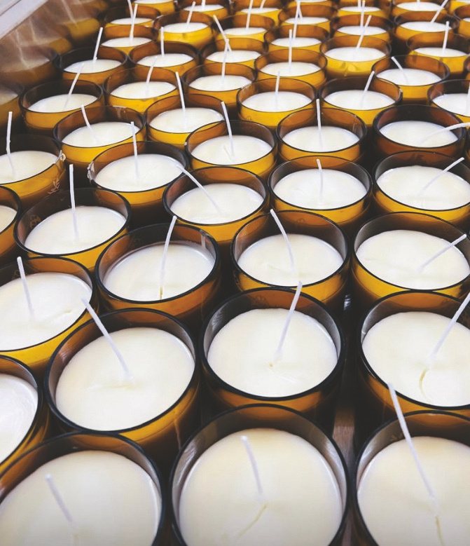 Rows of amber glass candle vessels, freshly poured, at the production partner's workshop