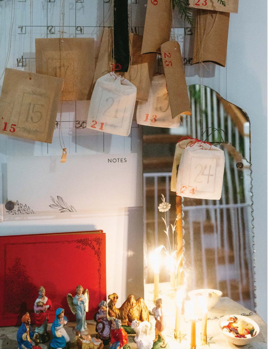 Small kraft envelopes of the handmade Advent calendar hanging above a row of lit candles