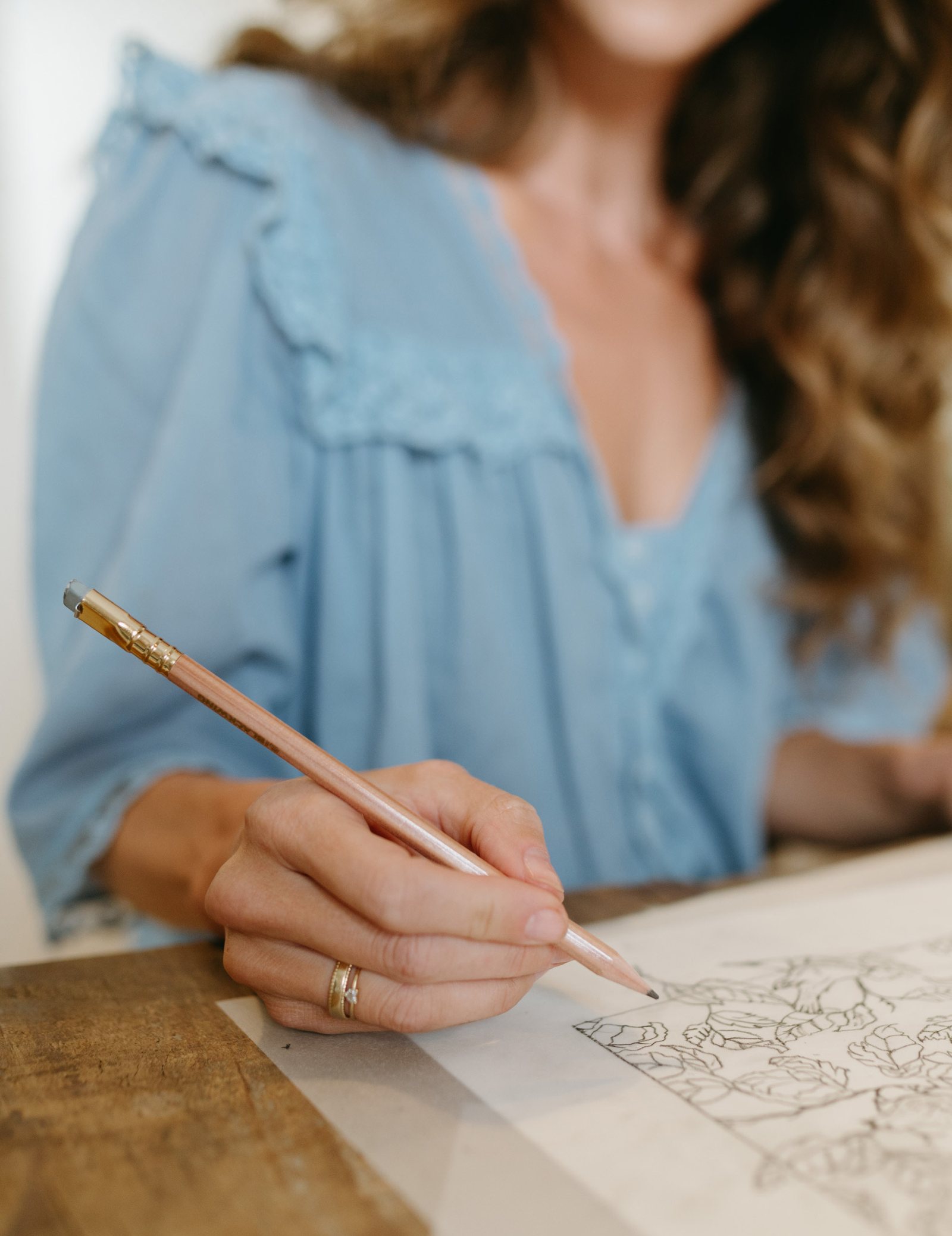 Bonnie Christine in a blue blouse sketching a floral motif in pencil