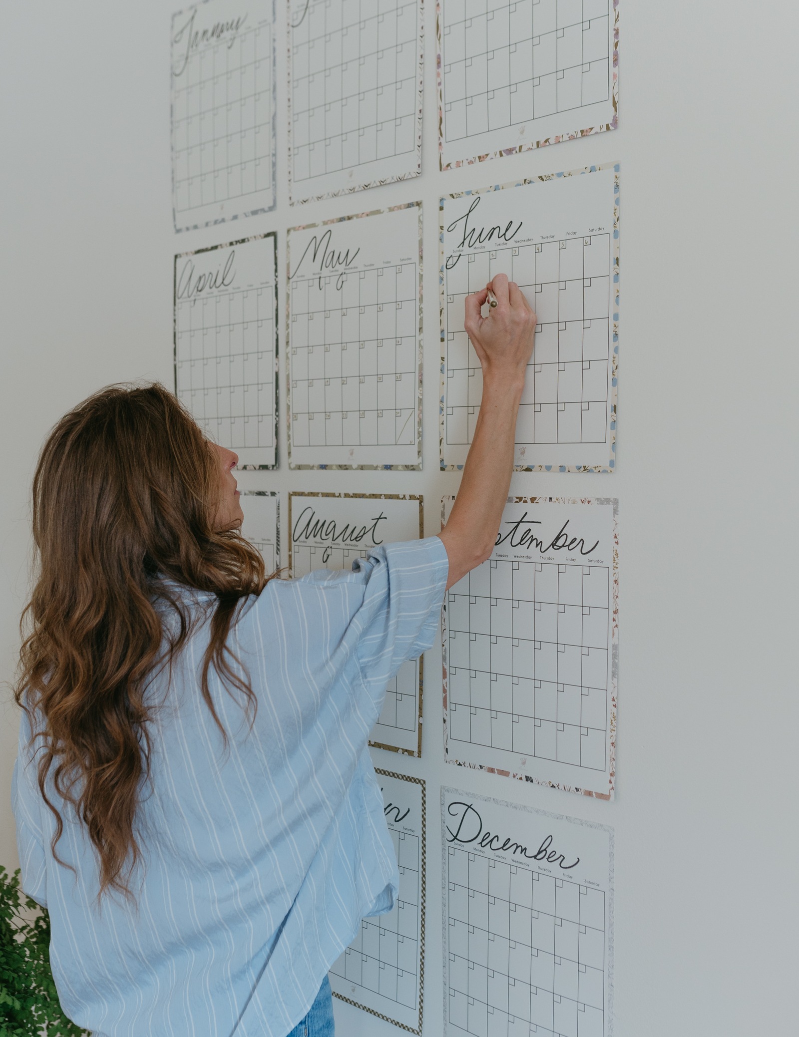 Bonnie Christine writing on a June calendar page in a wall of floral-bordered monthly calendars