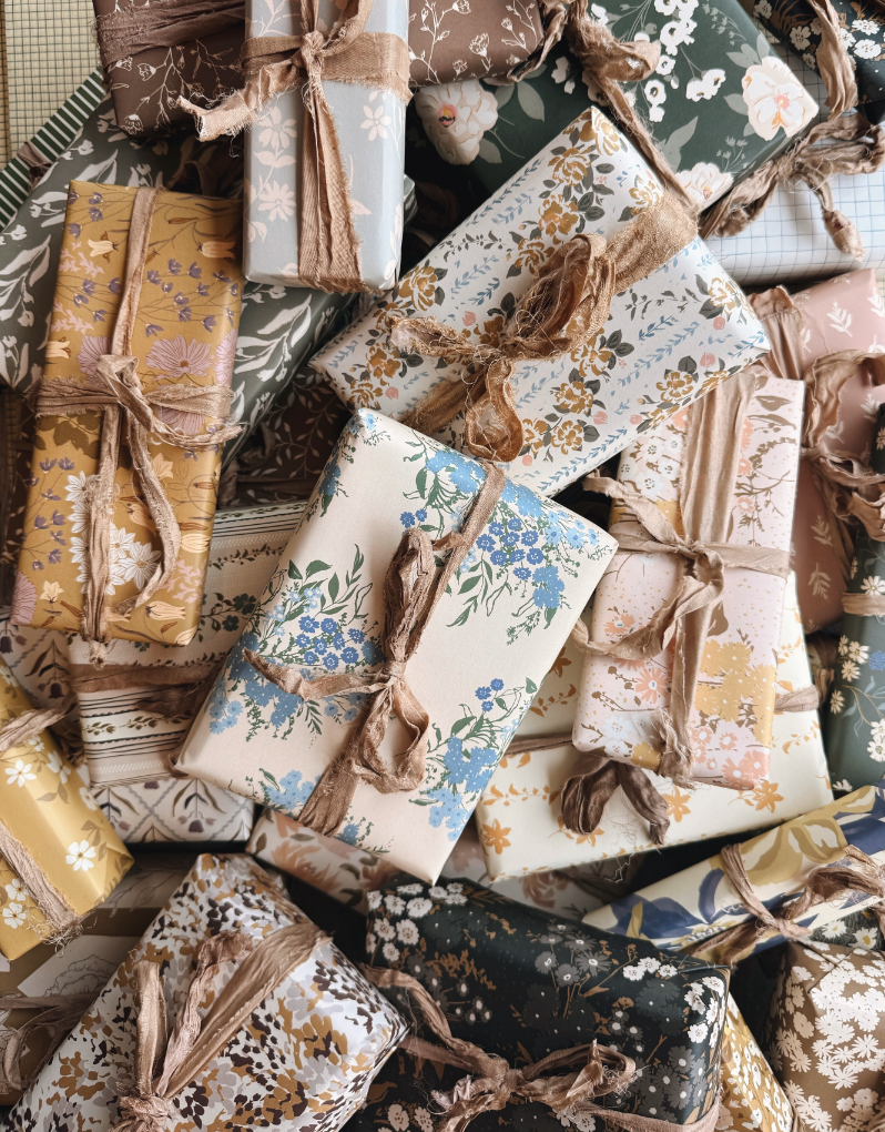 A pile of gifts wrapped in hand-designed floral papers tied with silk ribbon