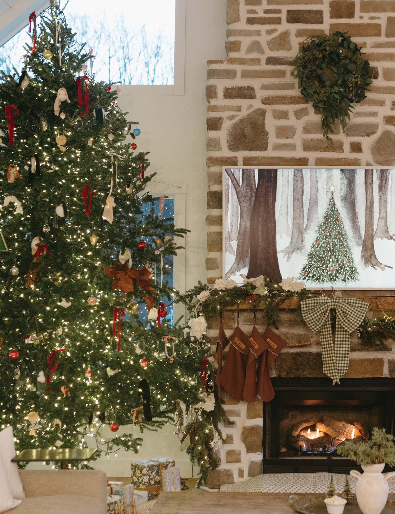 A Christmas tree beside a stone fireplace, stockings hung and a fire lit