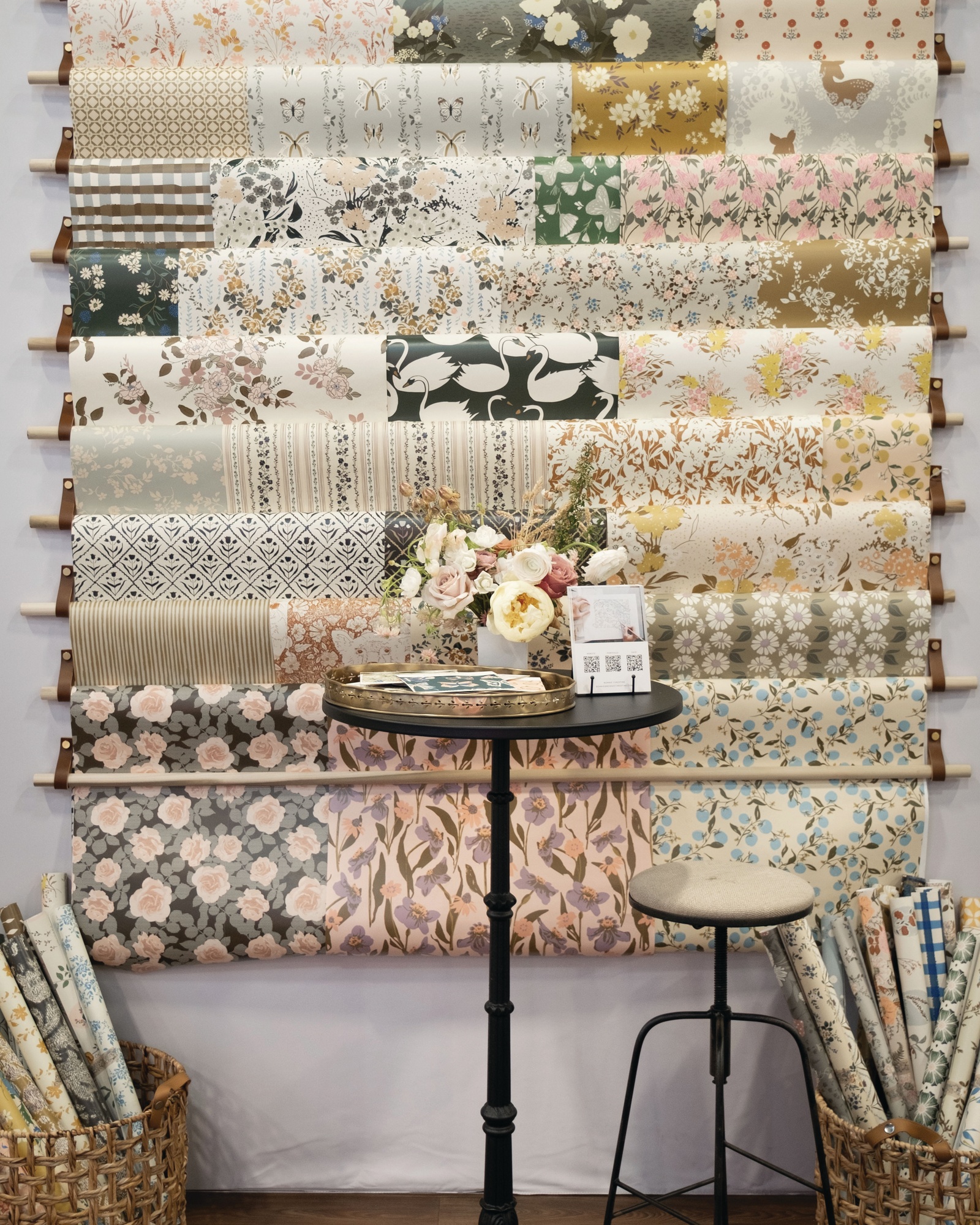 Bonnie Christine's Licensing Expo booth: a wall of fabric bolts above a bistro table and stools, with baskets of rolled fabric
