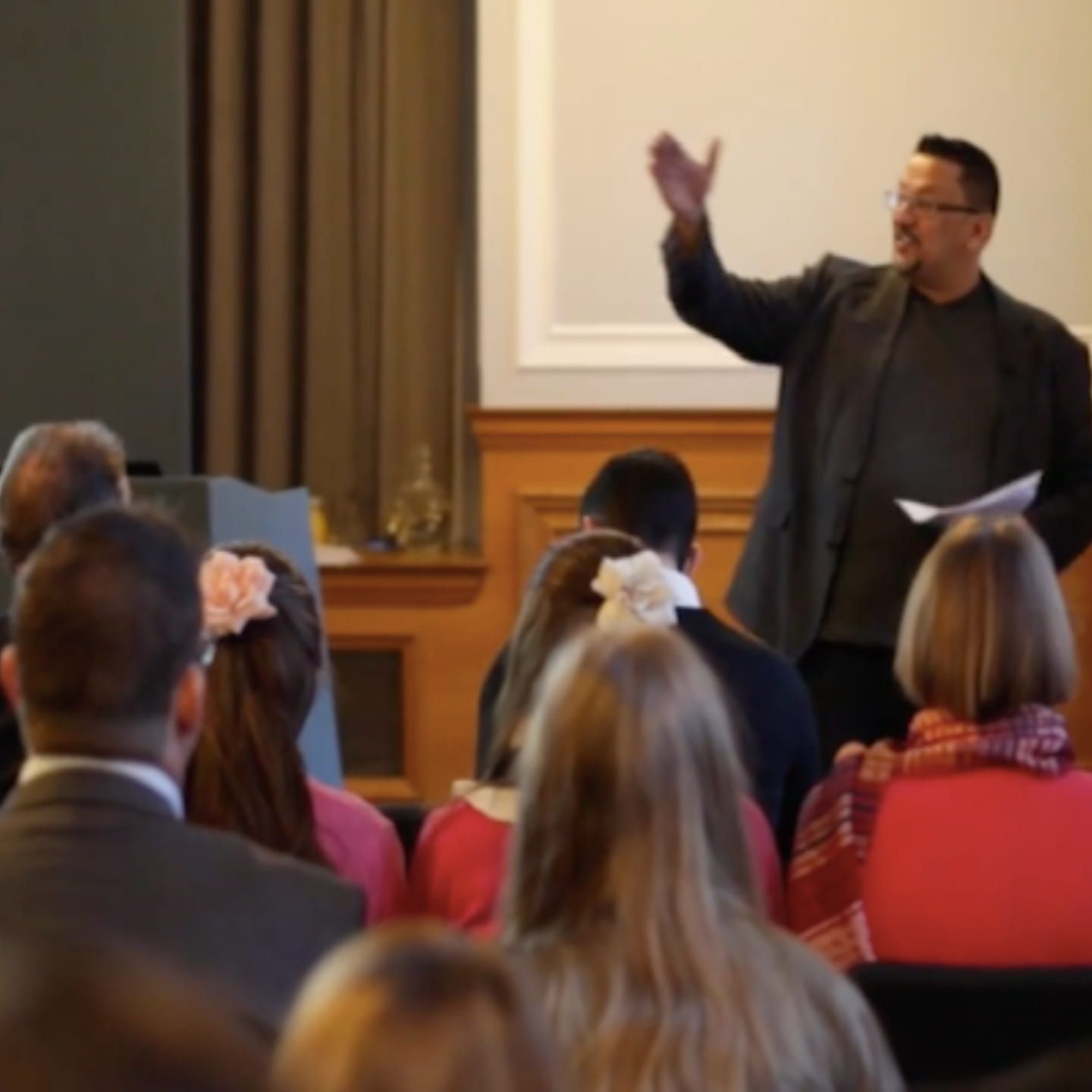 Roy Ripper speaking to an audience during a live business presentation, gesturing while holding notes at the front of the room.