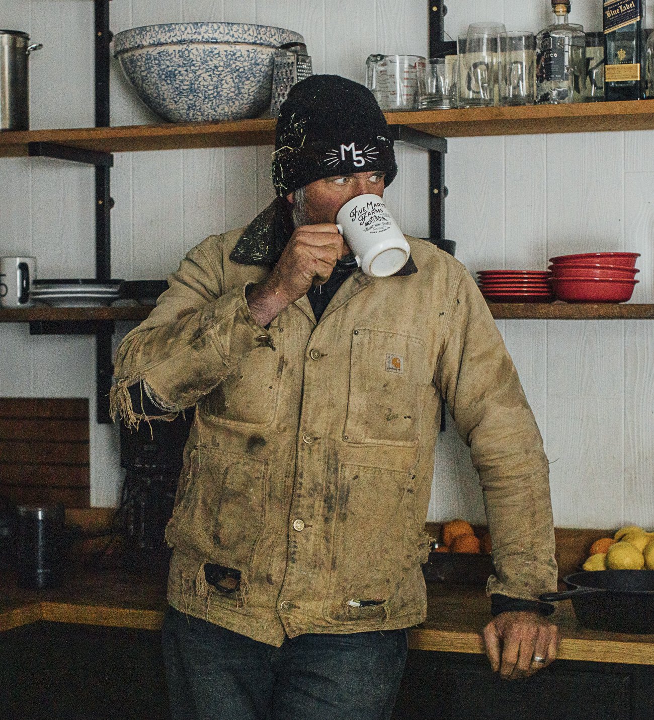 Brian Heffernan in a worn work jacket drinking coffee in the ranch kitchen