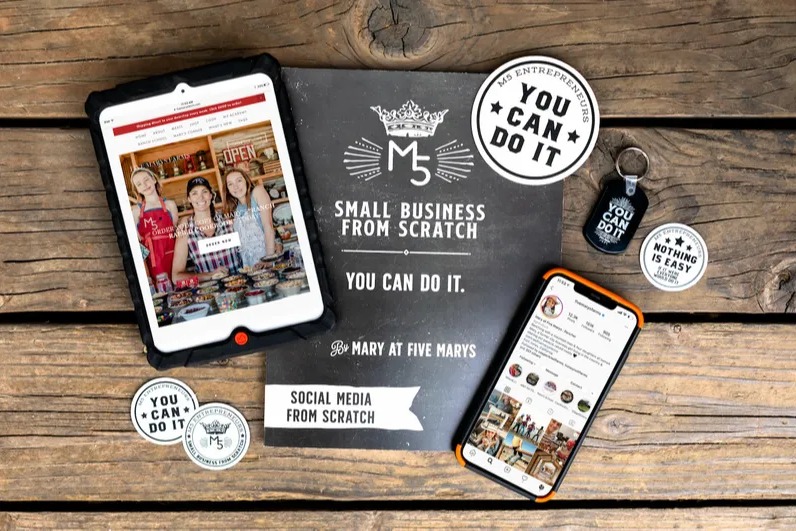 The original Social Media From Scratch workbook on a wood table with a tablet, a phone and You Can Do It stickers